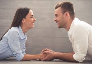 En la imagen se ve a una pareja el uno frente al otro, sonriéndose y dándose las manos